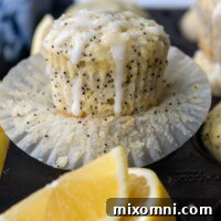 a lemon muffin with poppy seeds on an opened paper liner with glaze on top.