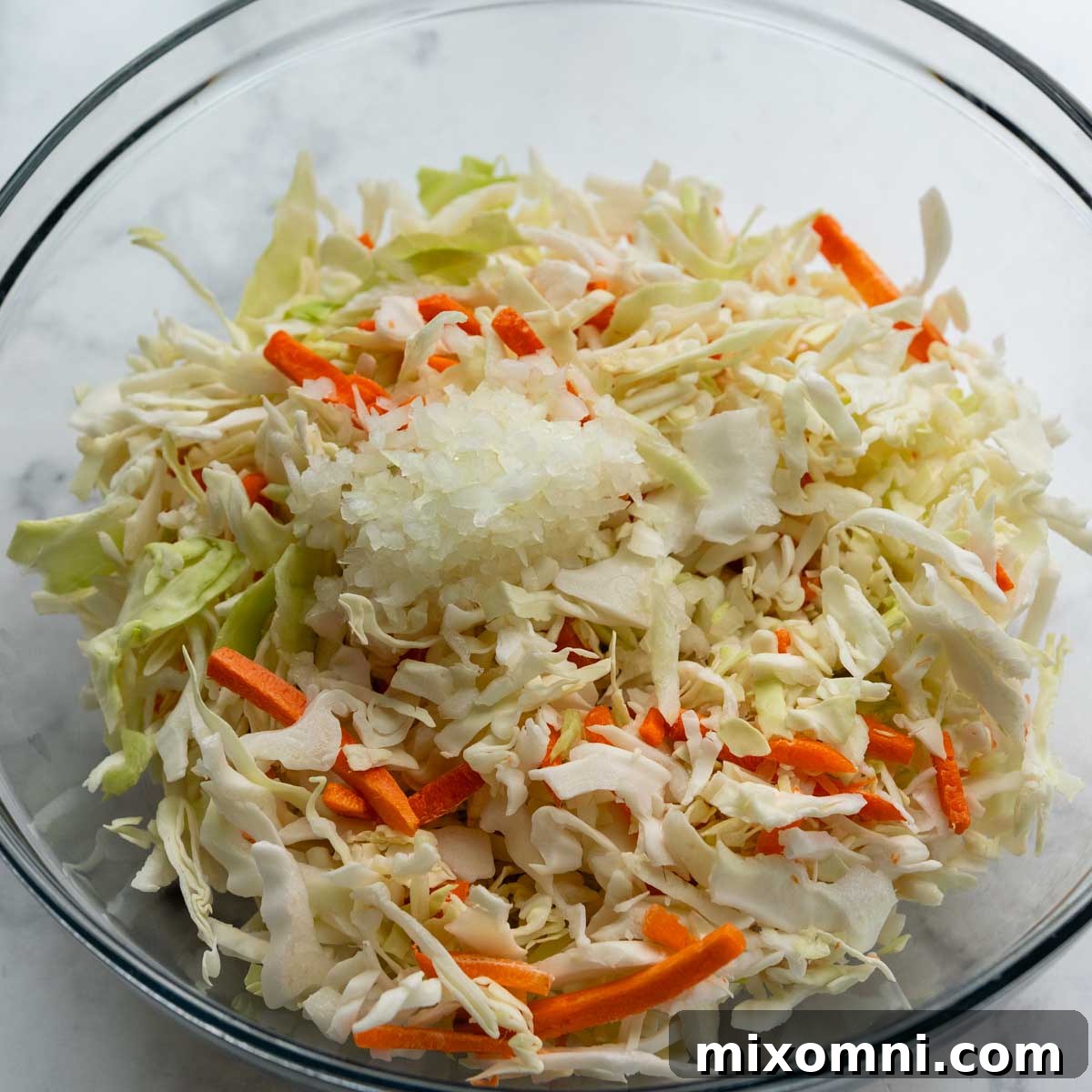 The coleslaw mix with minced onion, tossed with creamy dressing in a large bowl.