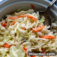 A spoon going into a bowl of coleslaw on a white marble surface.