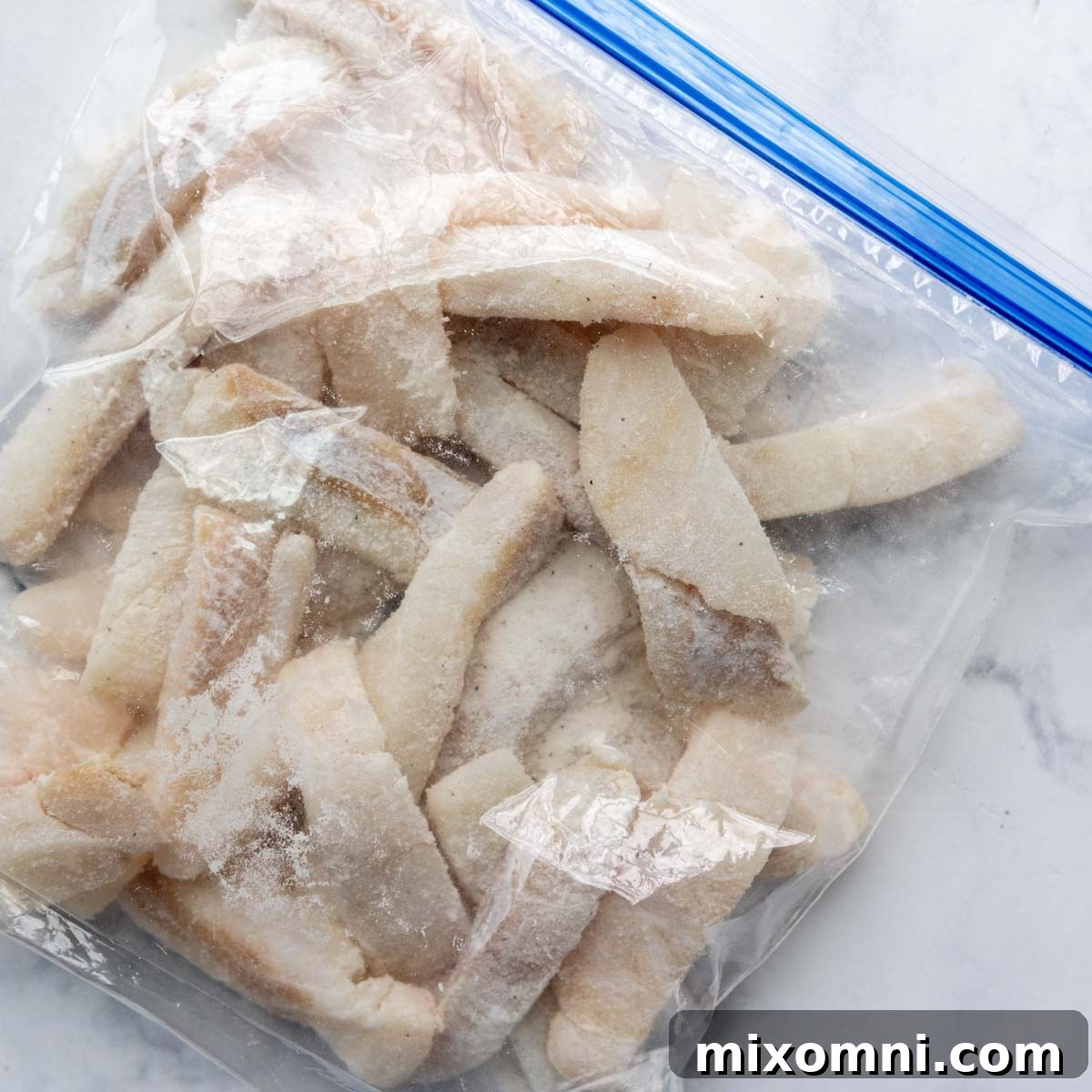 Pieces of white fish being dredged in a resealable plastic bag with a mixture of flour and seasonings, ensuring an even coating.