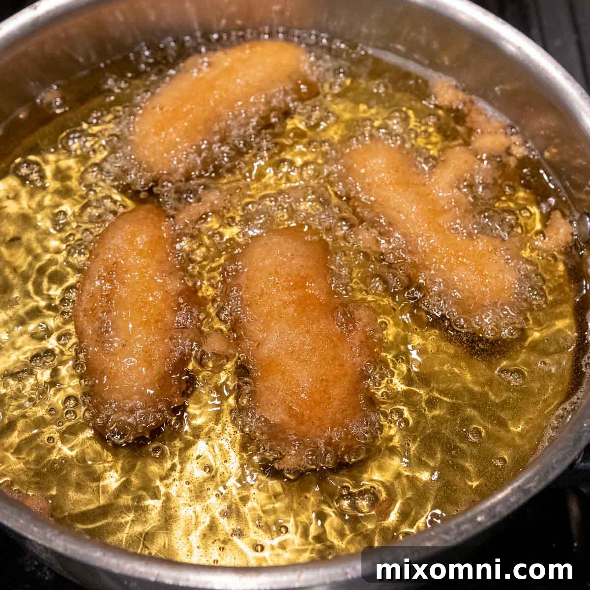 Several pieces of battered white fish sizzling and turning golden brown in hot oil within a deep skillet.