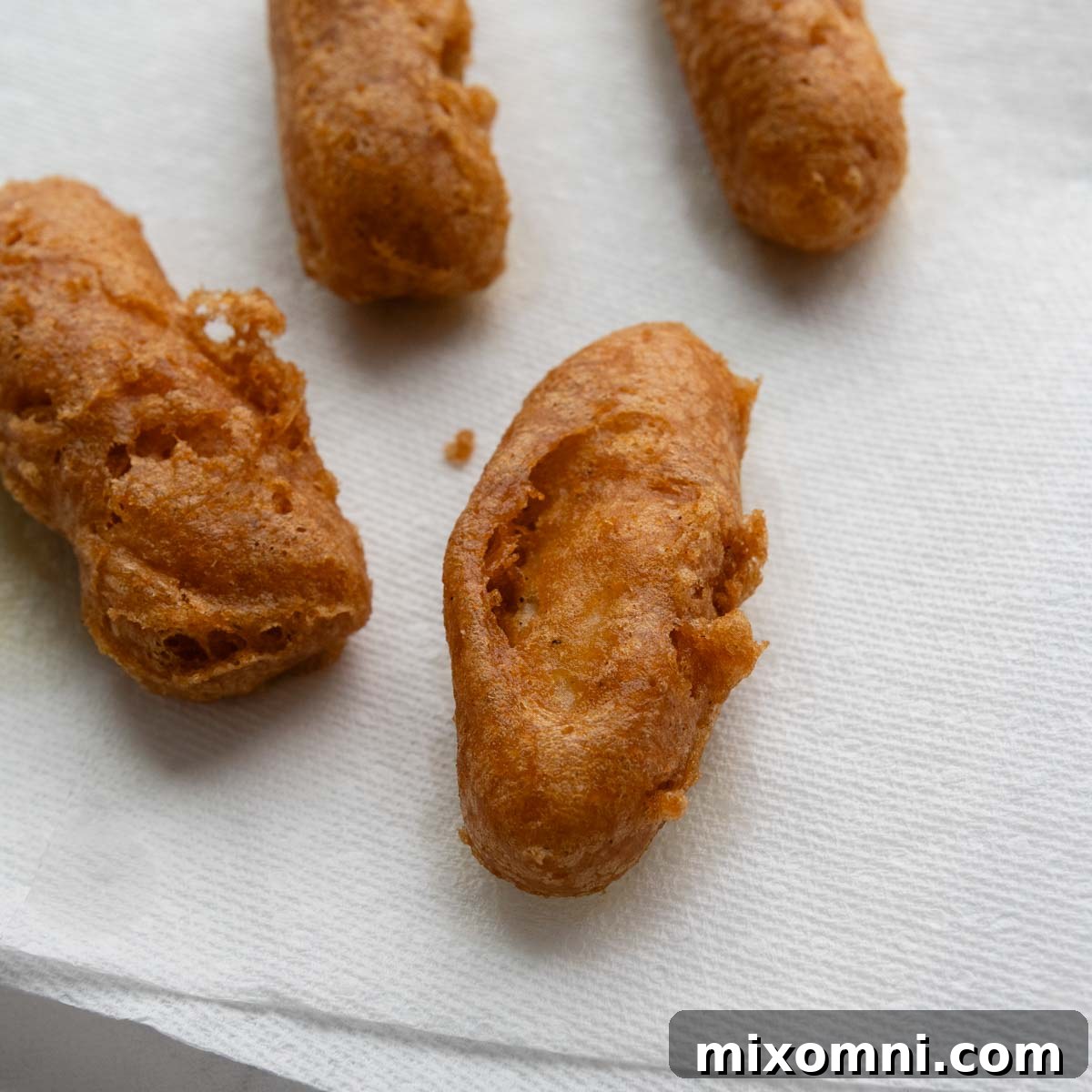 Freshly fried, golden-brown fish fillets resting on a paper towel-lined plate, absorbing excess oil before serving.