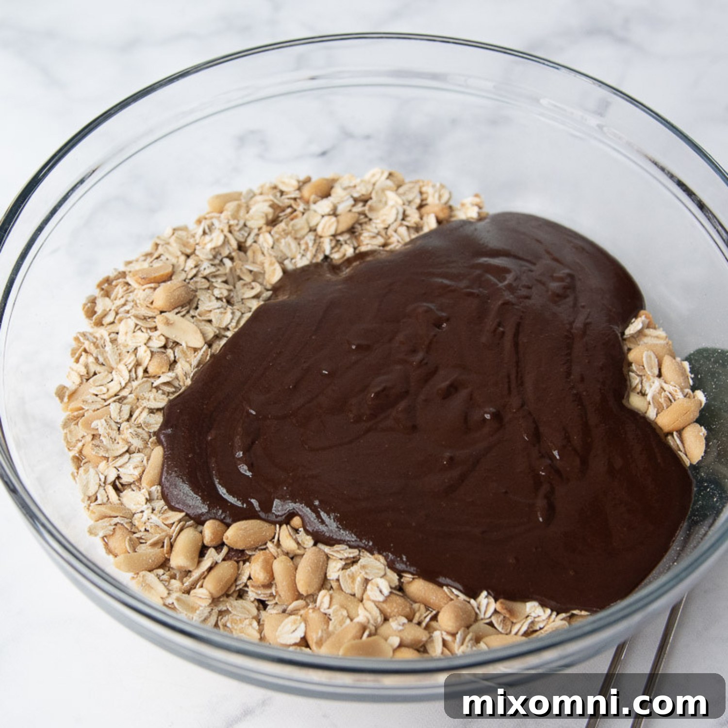 The chocolate coating being stirred into the oats in a large bowl, showing a rich, dark mixture.