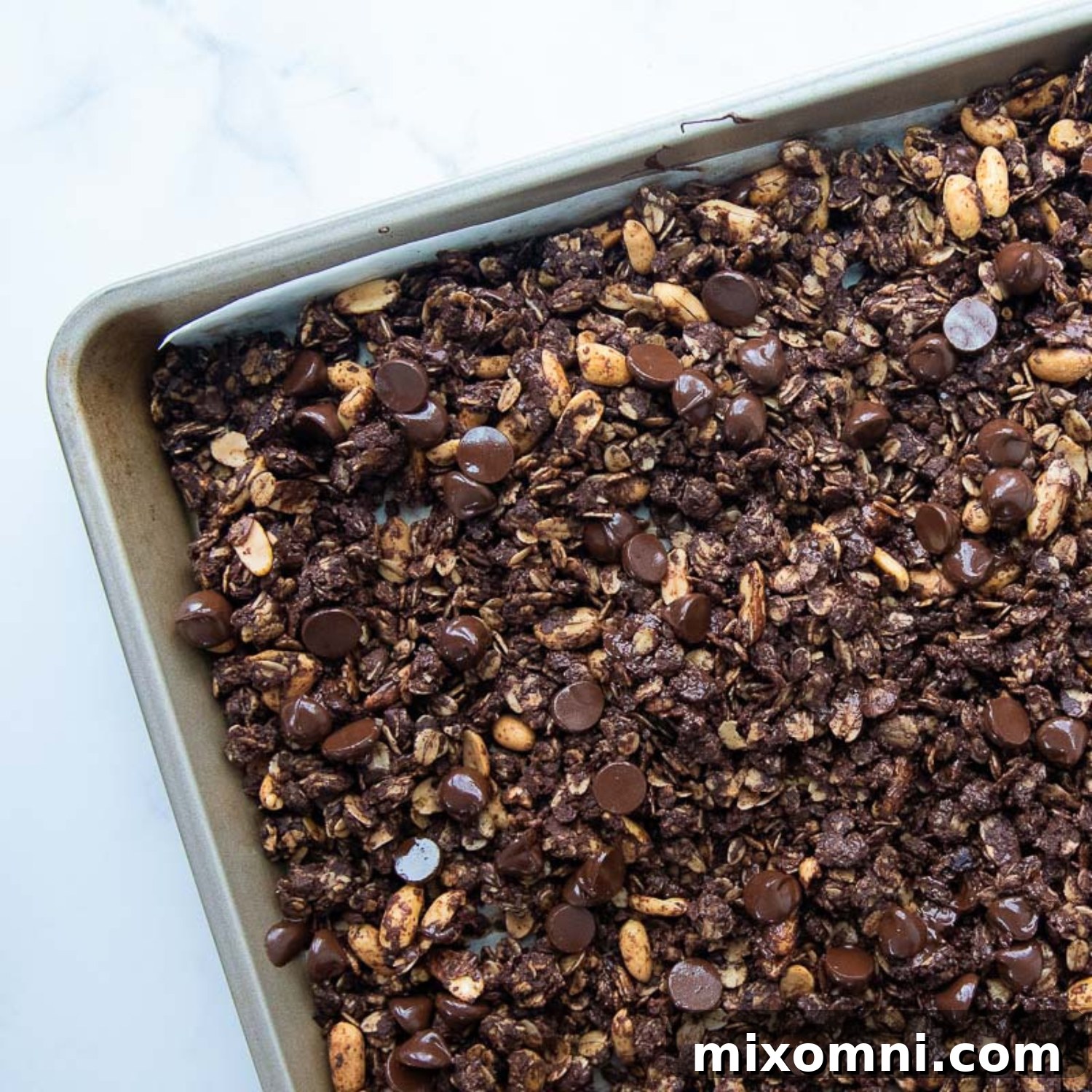 The baked granola on a baking sheet with chocolate chips melting on top, creating a rich glaze.