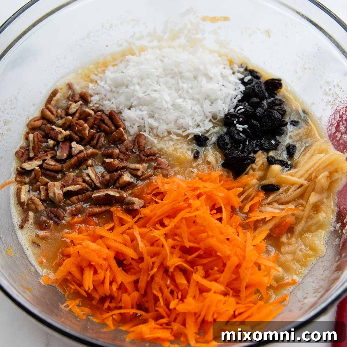 the wet ingredients in a bowl with grated carrots, apples, and other mix-ins added.