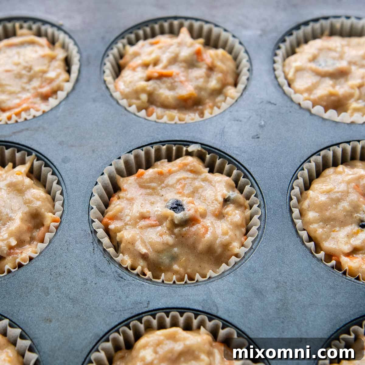 a muffin tin with liners filled almost to the top with unbaked batter, ready for the oven.