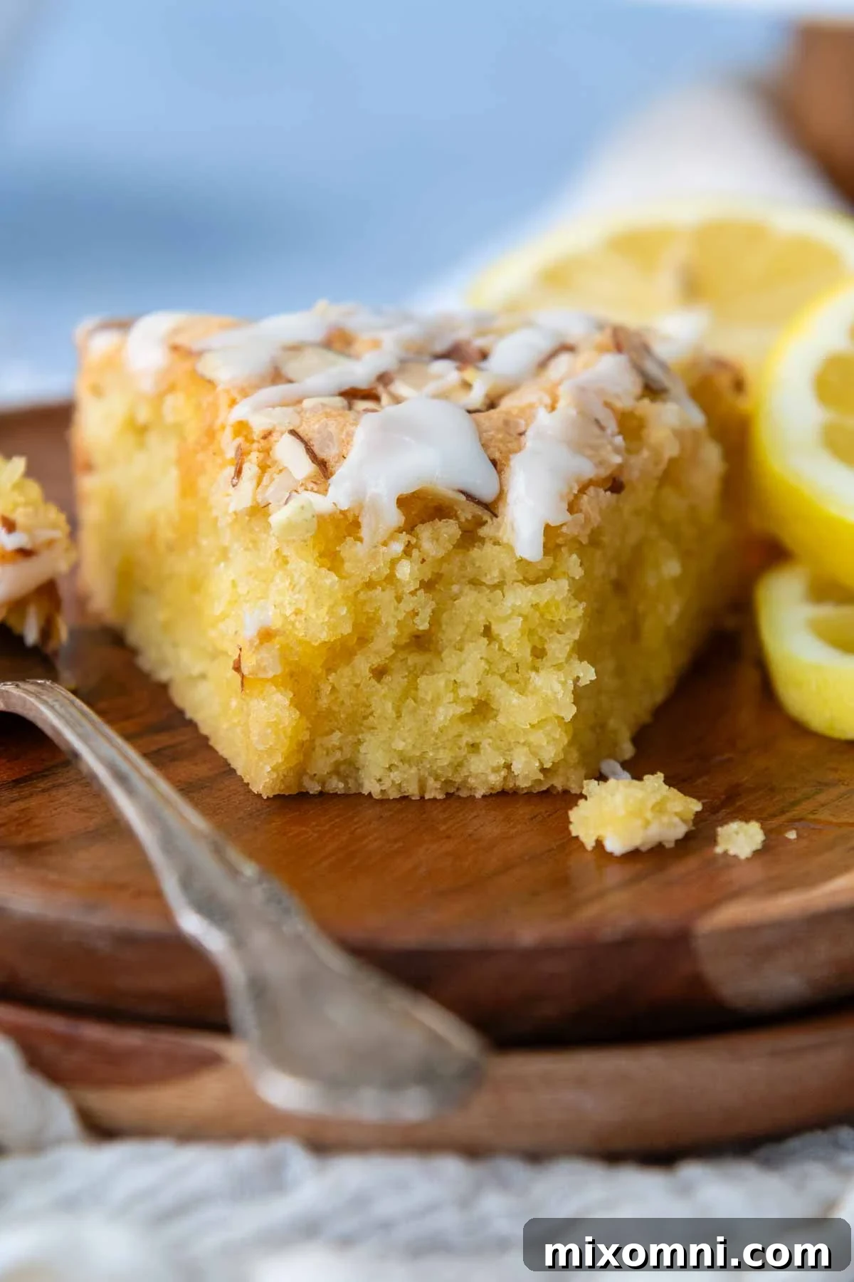 a slice of cake facing camera with a bite taken out and lemons on the plate.