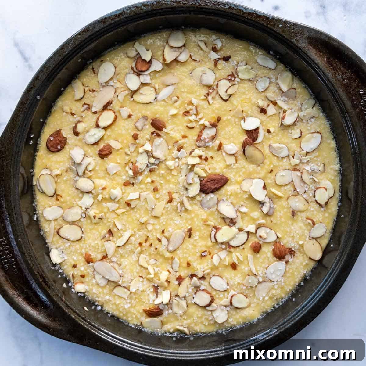 unbaked cake with sliced almonds and sugar on top.