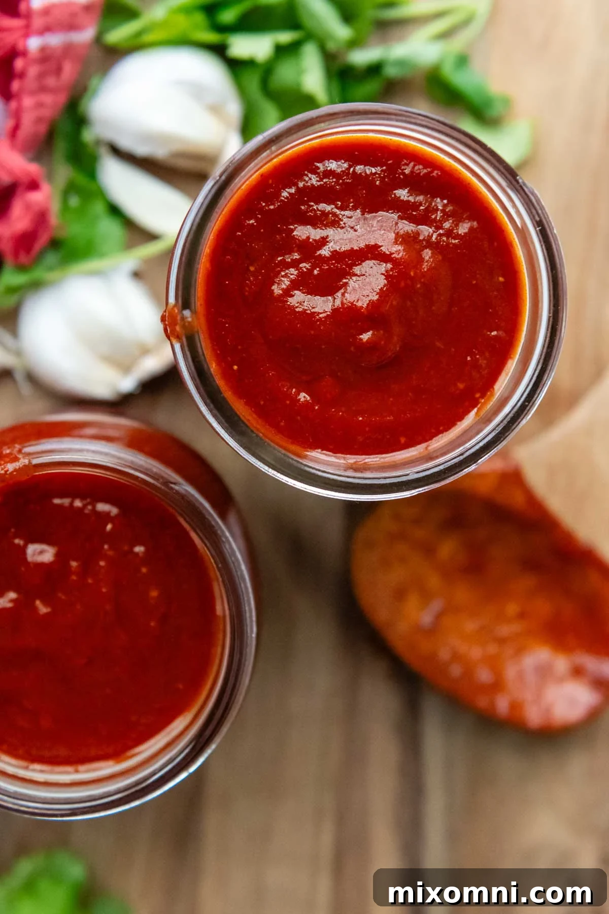 Two glass jars filled with vibrant red gluten-free enchilada sauce, with a wooden spoon resting nearby, against a rustic background.