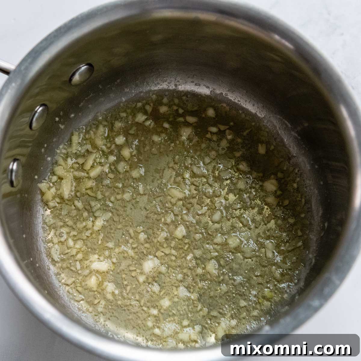 Minced garlic cloves being sautéed in melted butter within a saucepan.