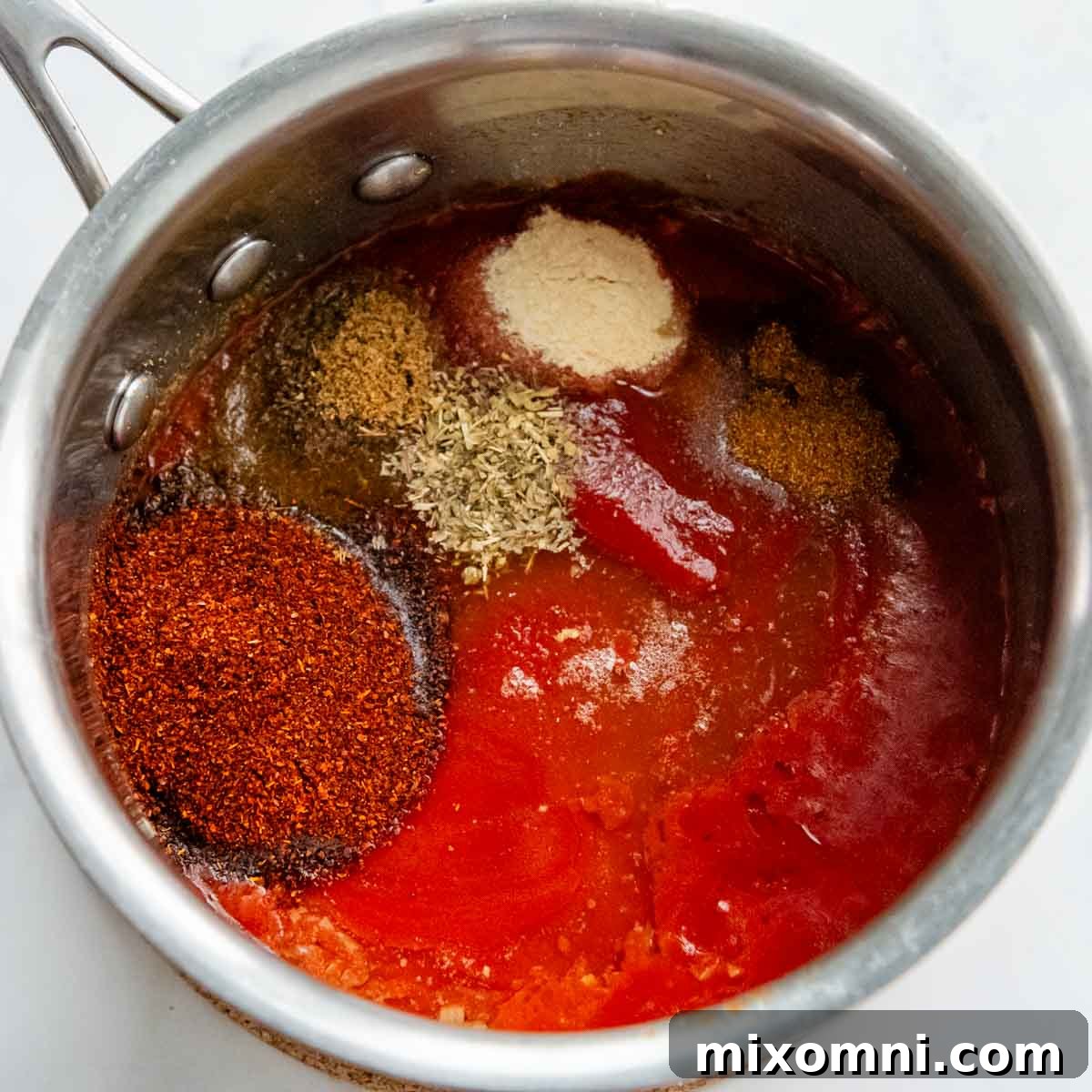 Canned tomato sauce, apple cider vinegar, and various spices being added to a saucepan.