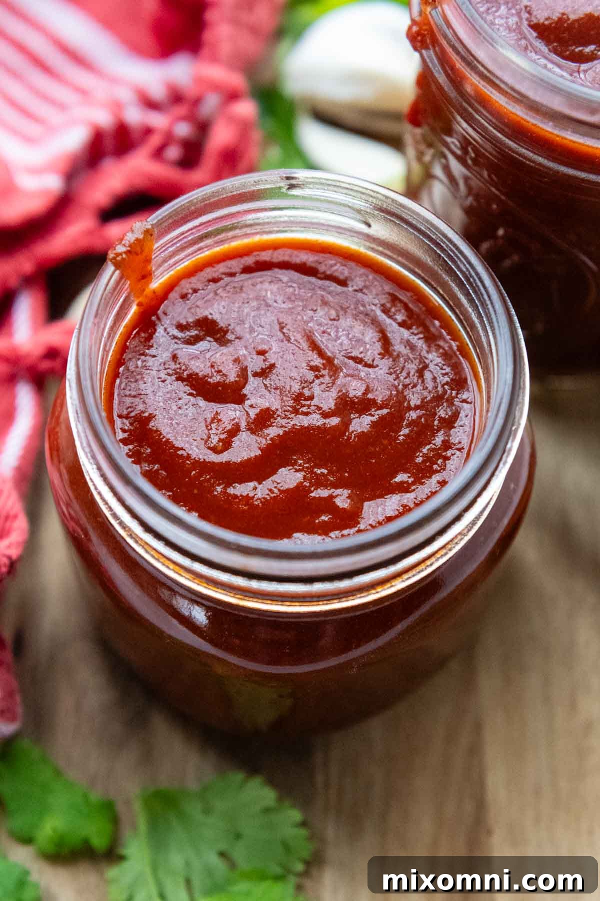 A close-up top-down view of vibrant red enchilada sauce in a clear glass jar, ready for storage.