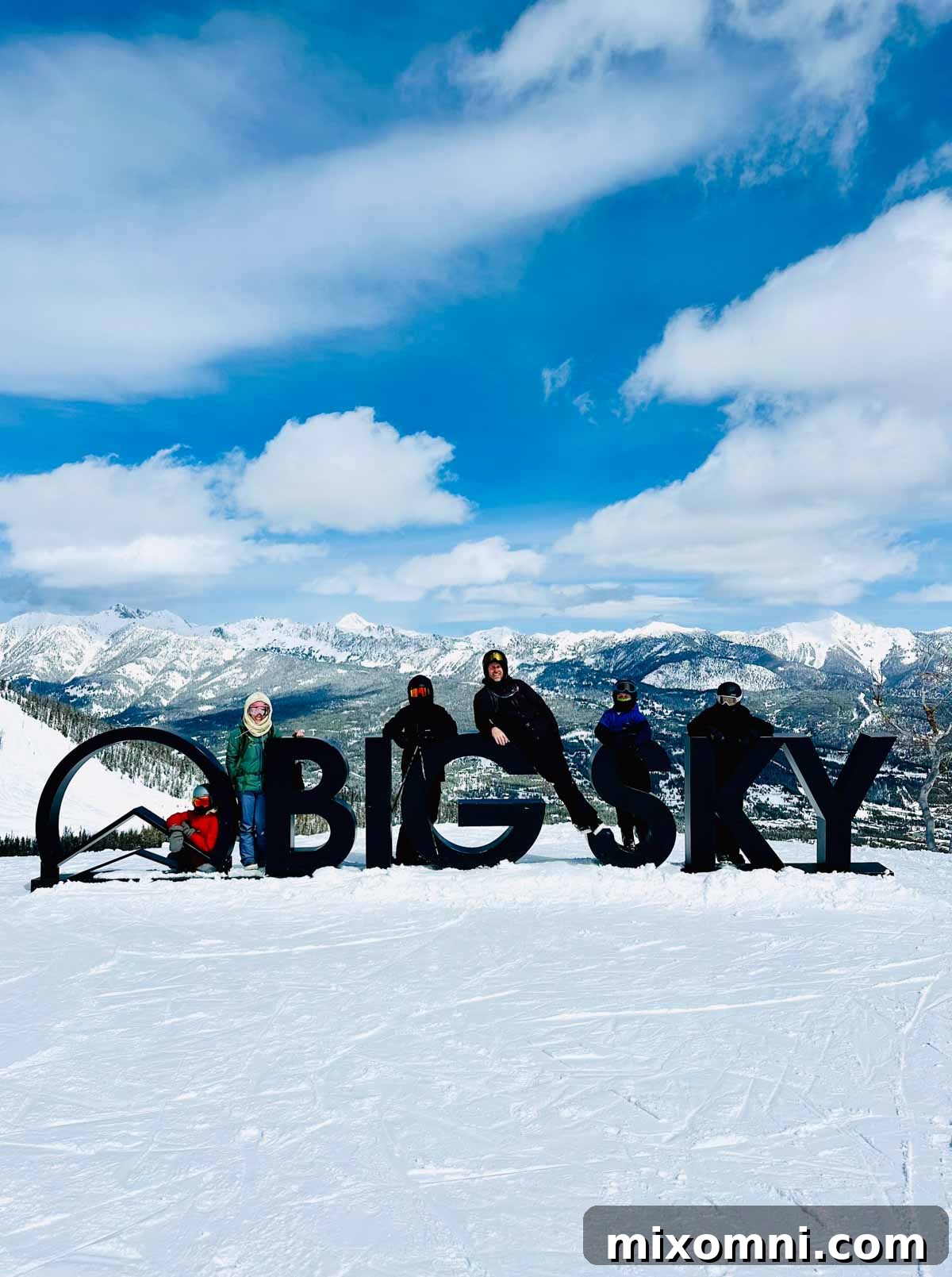 Family posing by a Big Sky sign with snow-capped mountains in the background.