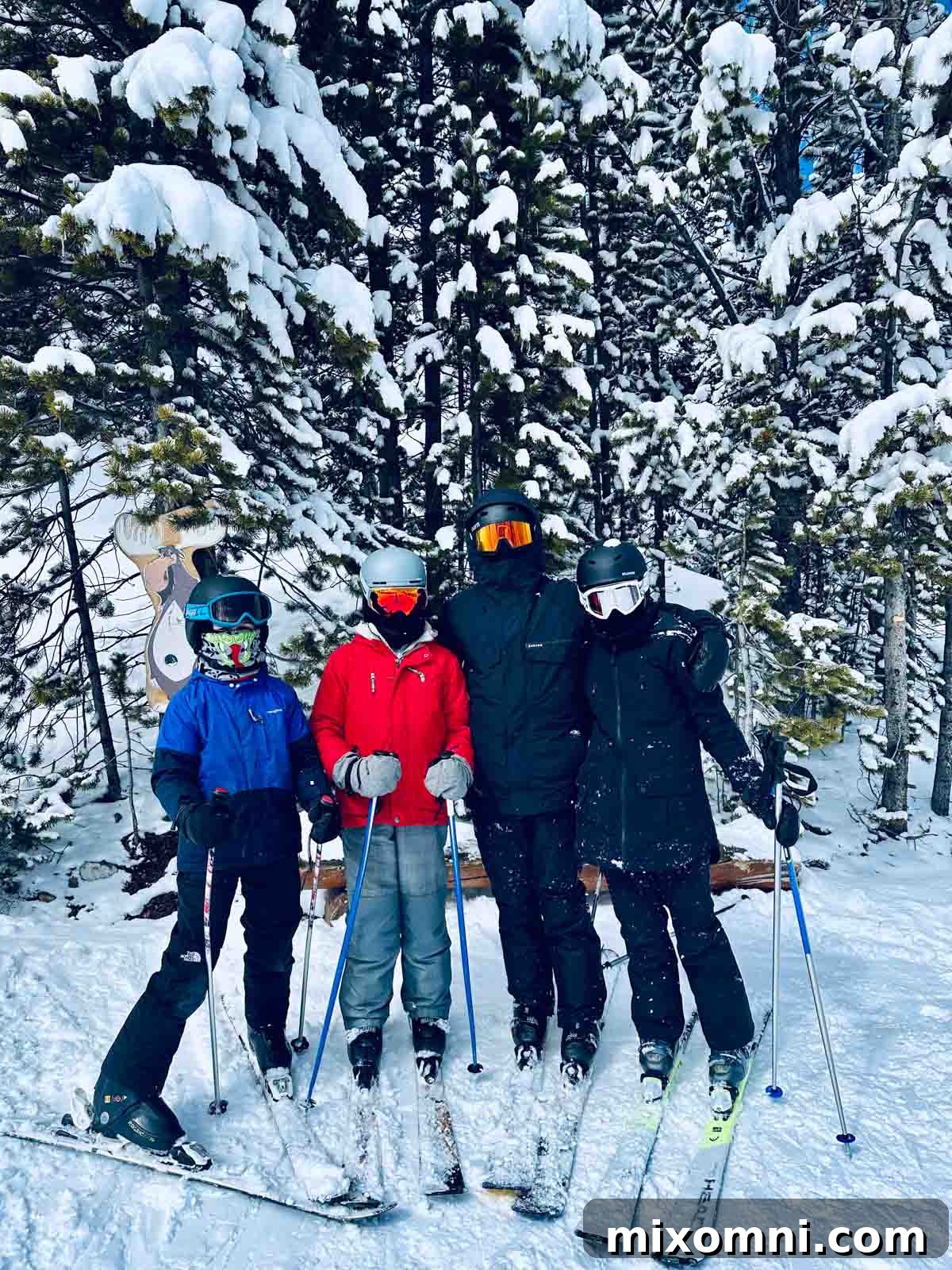 Kids posing on a snowy ski run with pine trees and blue sky.