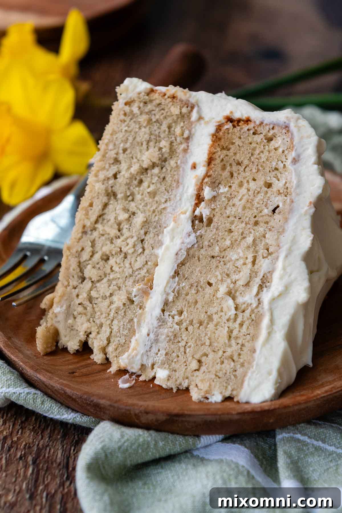 A beautiful slice of gluten-free banana cake on a rustic wooden plate, highlighting its tender texture and smooth frosting.