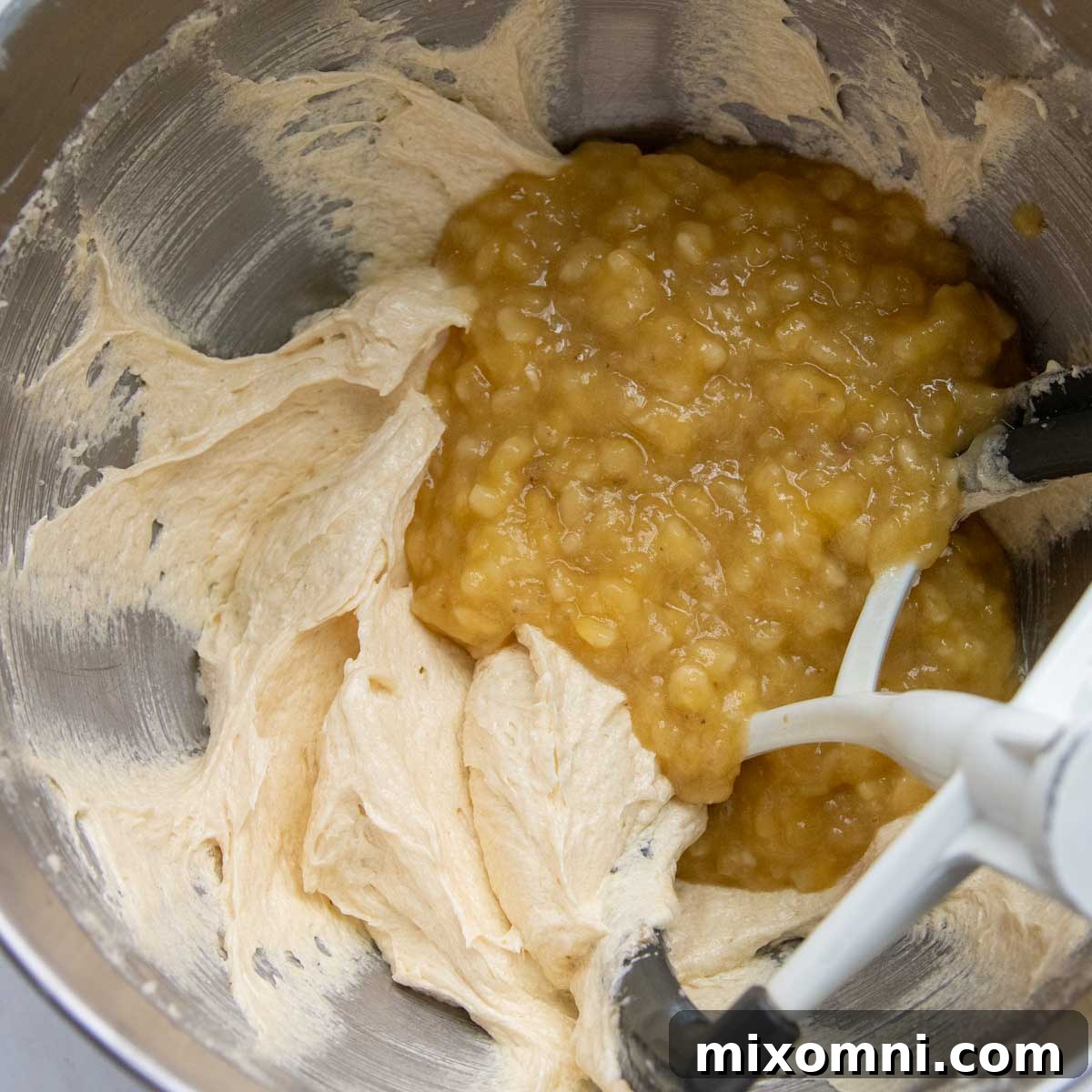 Mashed ripe bananas being gently folded into the cake batter along with eggs and extracts.