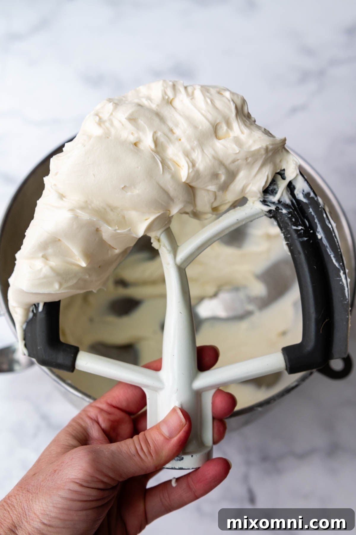 A whisk attachment covered in light and fluffy whipped cream cheese frosting, ready to spread on the cake.