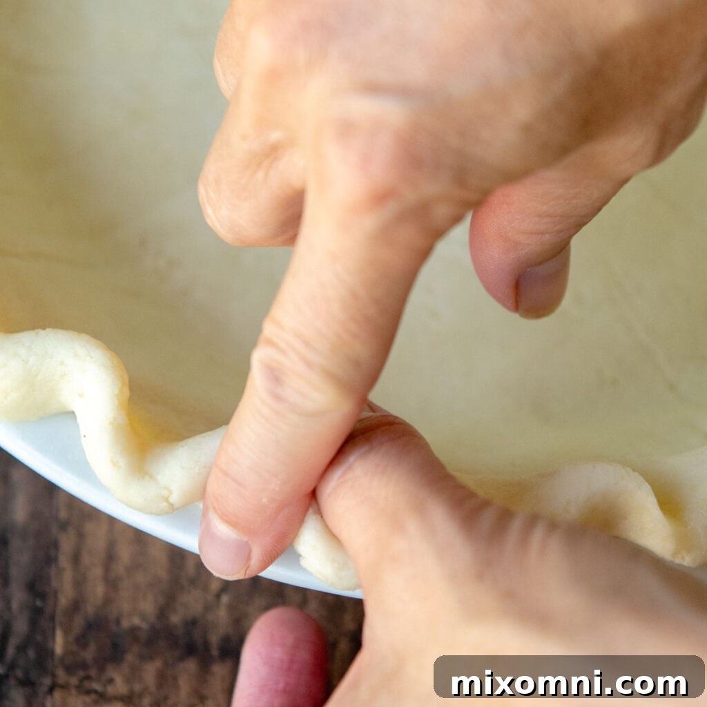 Hands crimping the edges of a pie crust into a decorative flute pattern.