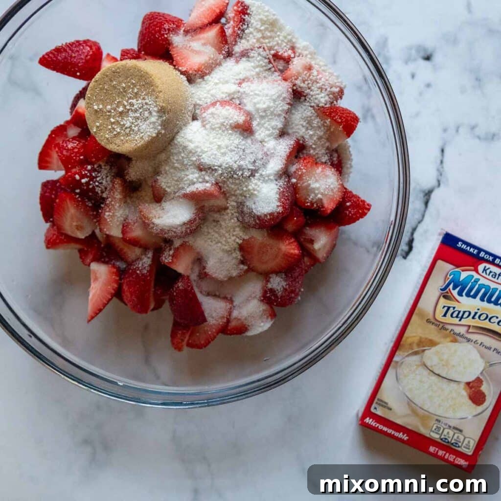 Bowl containing fresh strawberries, sugars, and lemon juice for the filling, with a box of instant tapioca visible beside it.