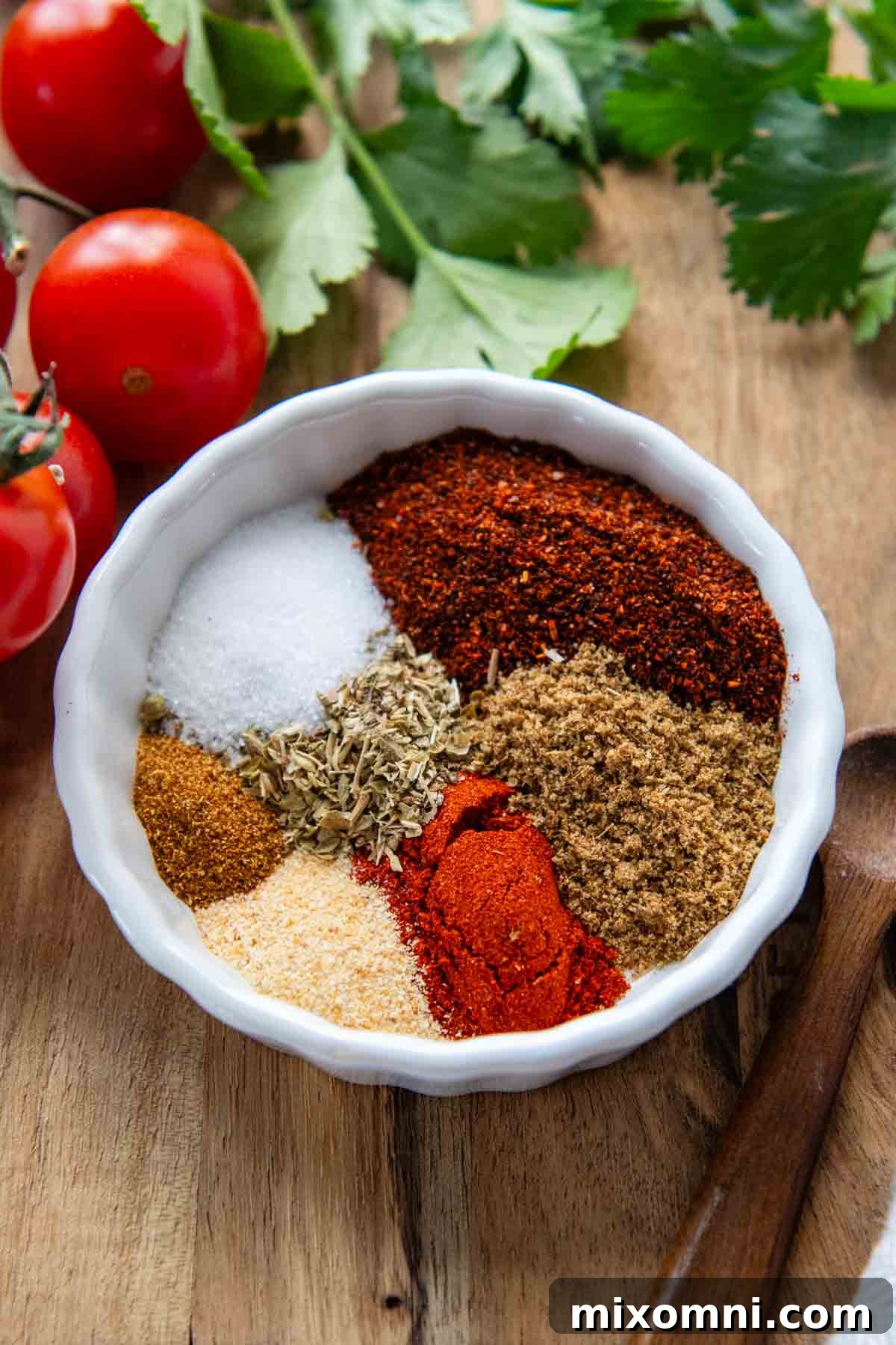 A small white bowl filled with a blend of taco spices, with fresh cherry tomatoes resting beside it.