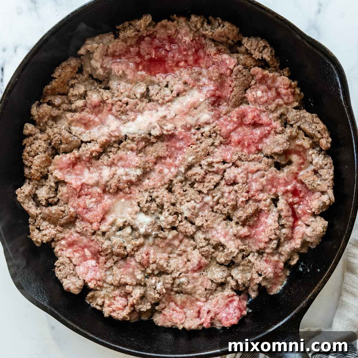 Ground beef cooking in a hot iron skillet, pressed into a single layer for optimal browning.