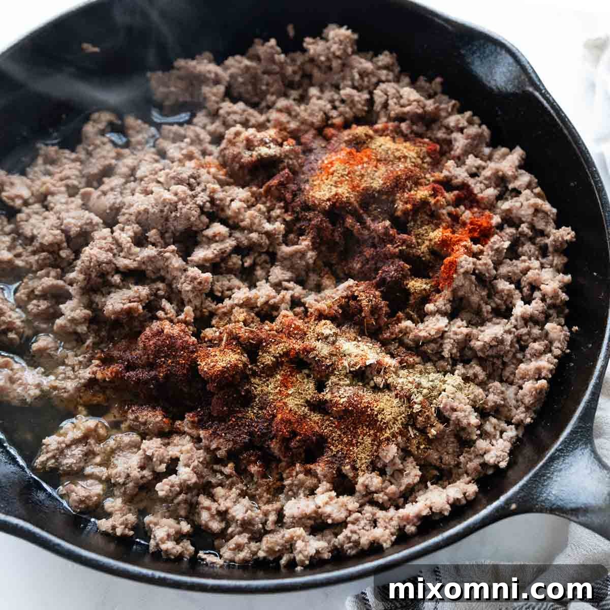 Taco meat in a skillet, with homemade taco seasonings generously sprinkled over the top, ready to be stirred.