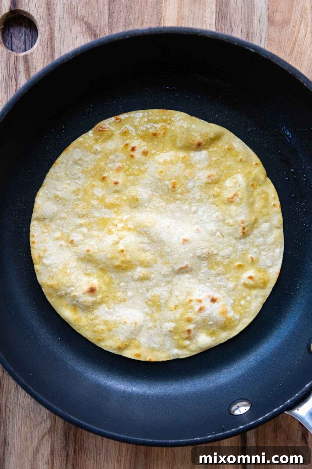 A corn tortilla being warmed in a frying pan, becoming pliable and slightly toasted.