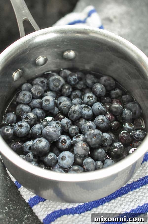 A small pot of blueberries partially covered with water and maple syrup, simmering on the stove.