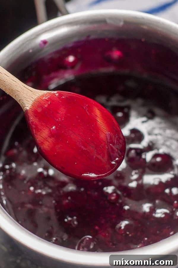 The back of a wooden spoon coated with blueberry syrup, illustrating the perfect thickness.