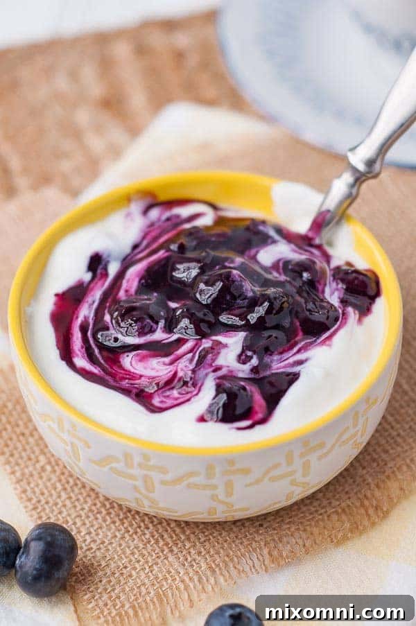 Vibrant blueberry syrup swirled into a small bowl of creamy yogurt, ready to be enjoyed.