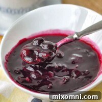 A bowl of blueberry syrup with a spoon resting on side