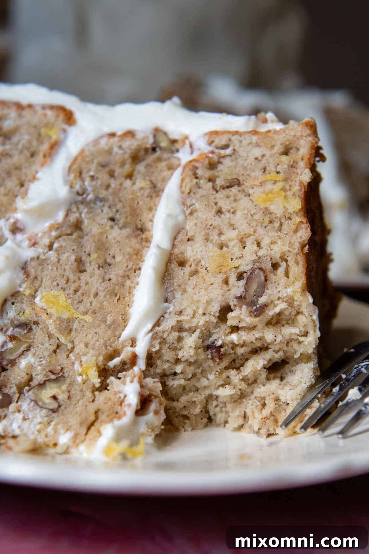 A perfectly sliced gluten-free hummingbird cake on a white plate, revealing its moist layers and creamy frosting, with a bite taken out.