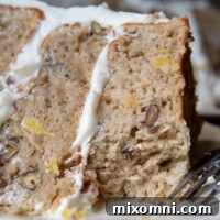 A slice of gluten-free hummingbird cake on a white plate with a bite taken out, close up.