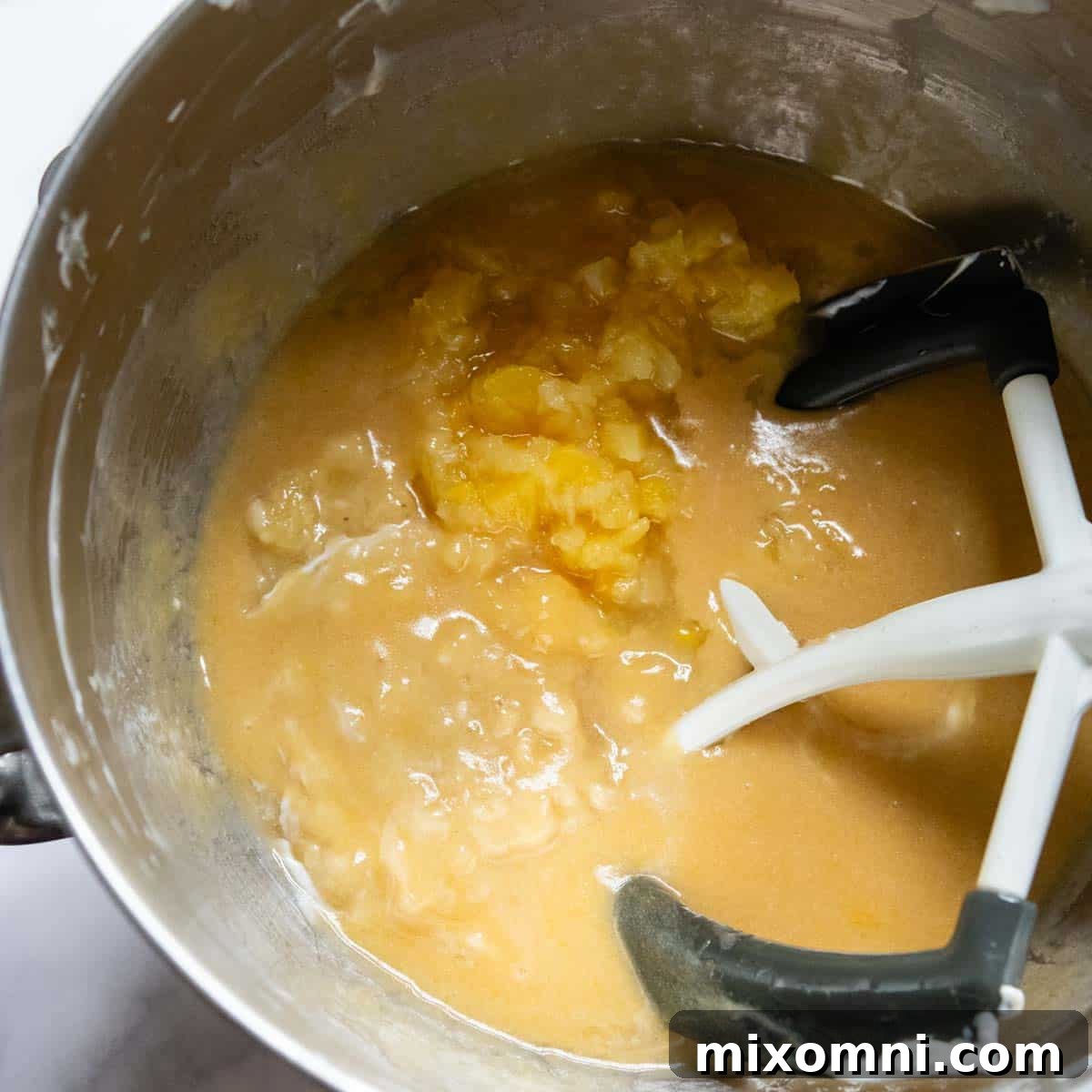Crushed pineapple and mashed bananas added to the creamy cake batter, ready to be mixed.
