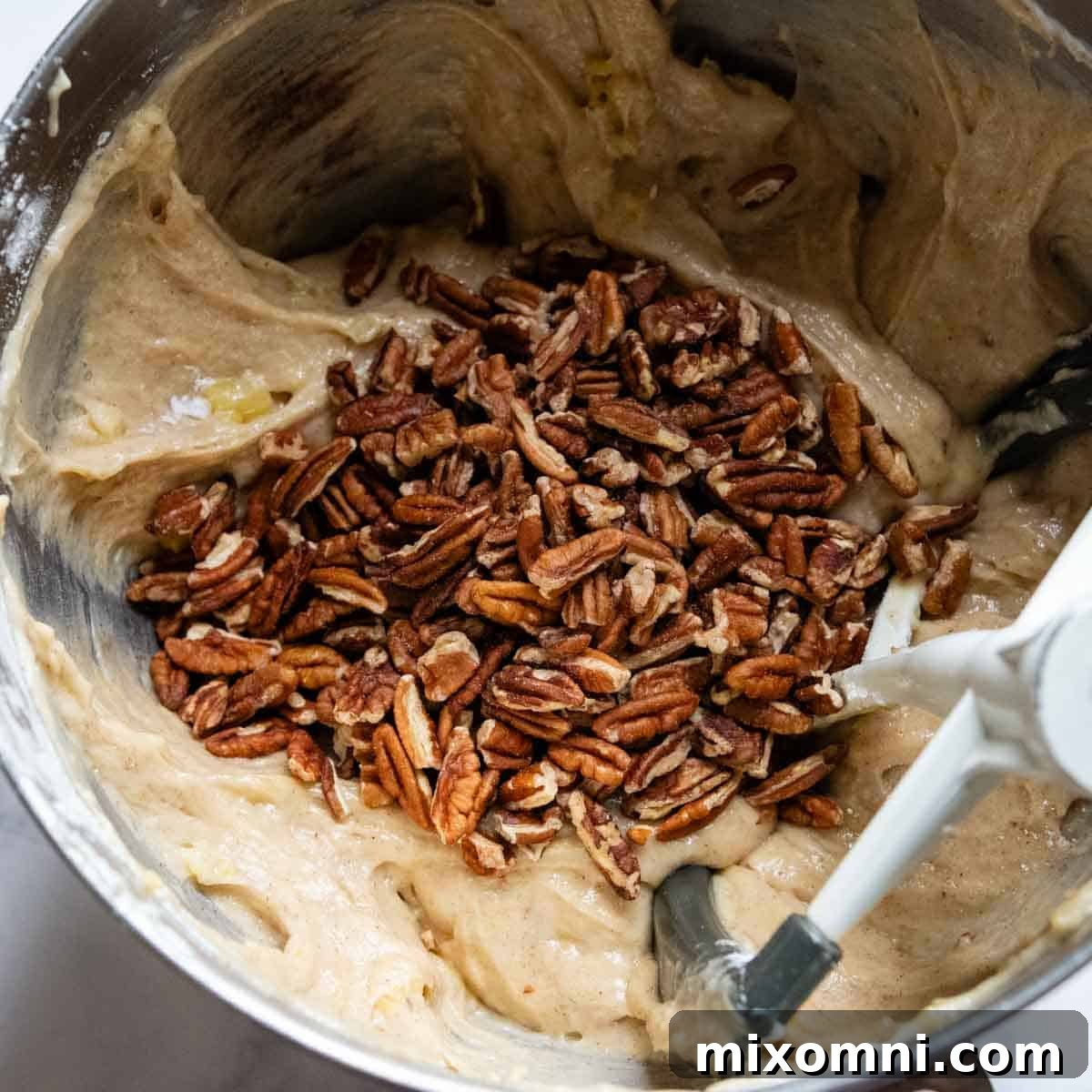 Chopped pecans added to the thick, spiced cake batter, ready for a final mix.