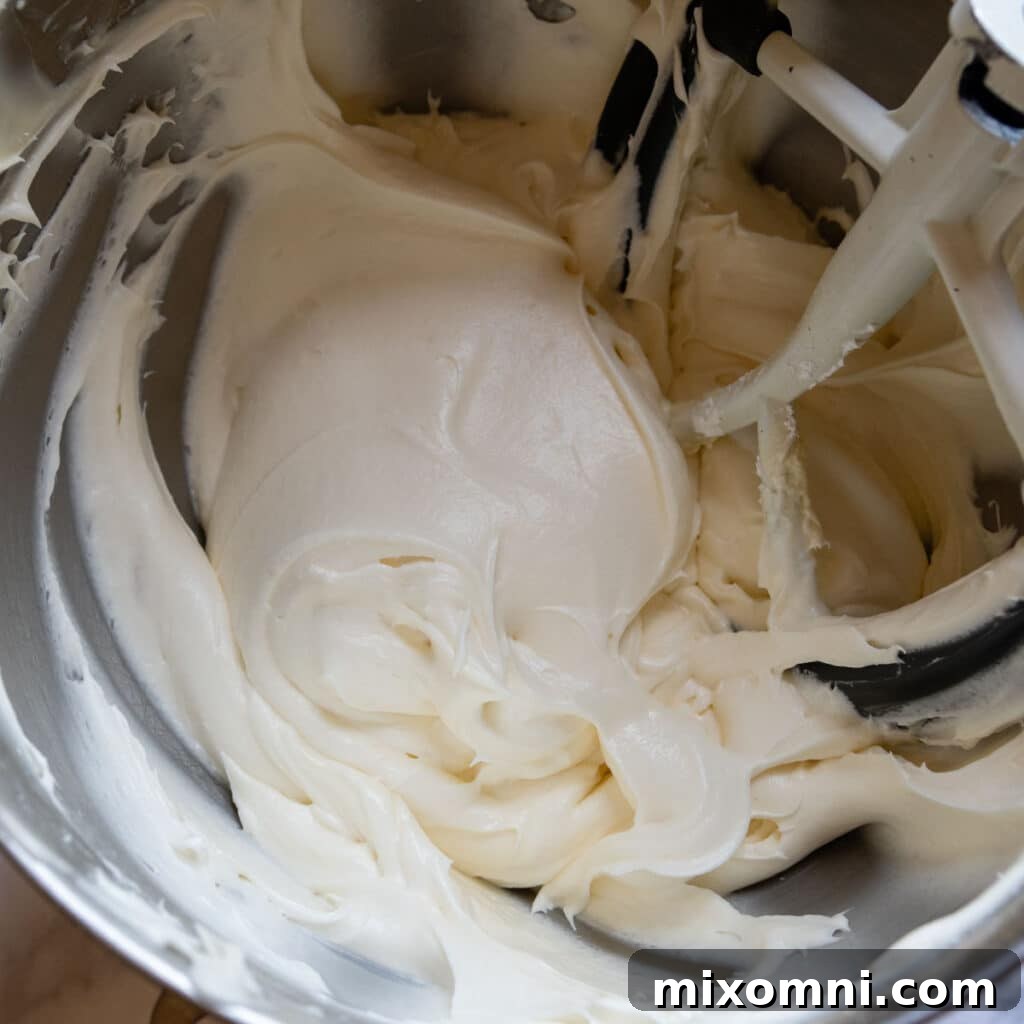 Cream cheese frosting being beaten to a light and fluffy, whipped cream-like texture in a mixing bowl.