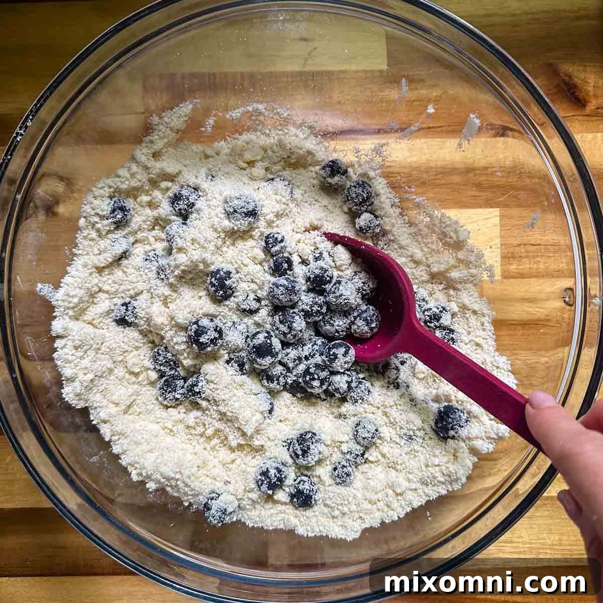 Fresh blueberries being mixed into the sandy almond flour and butter mixture.
