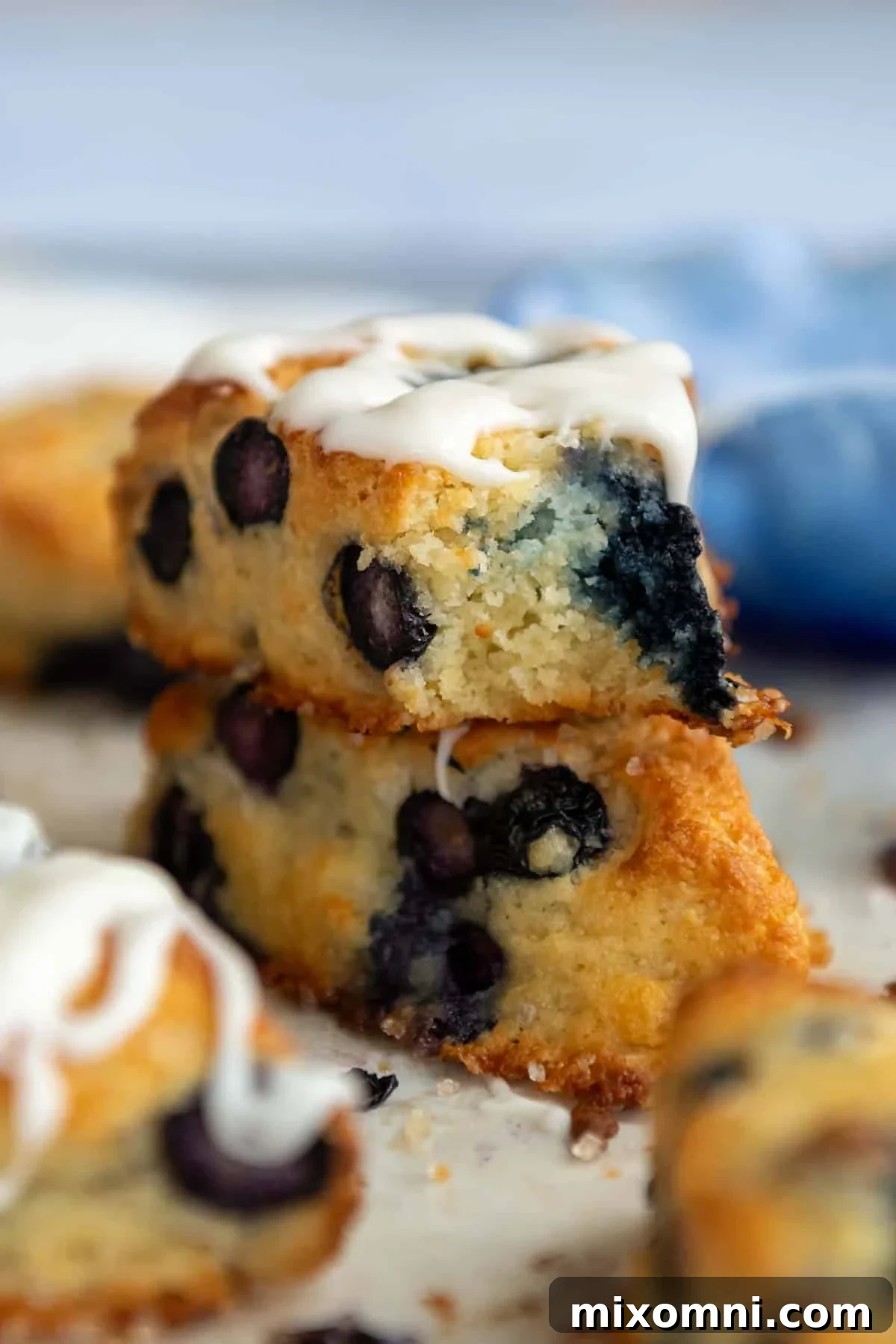 A stack of two perfectly baked almond flour scones, with the top one showing a bite taken out and a delicate glaze.
