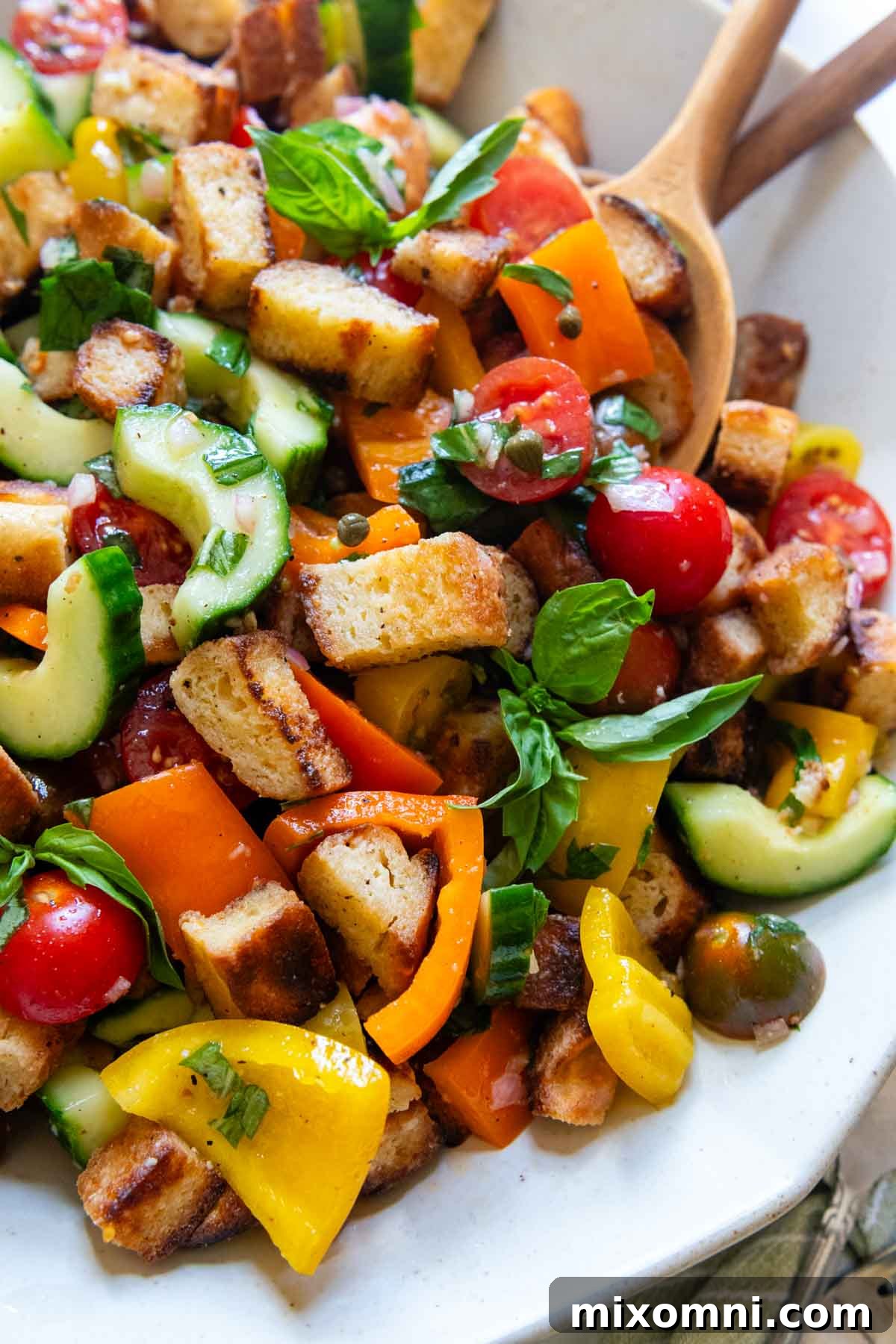 close up of panzanella on a white serving platter with utensils on the side.