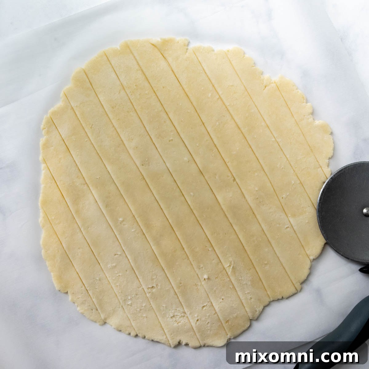 Precisely sliced gluten-free pie crust strips, laid out on parchment paper, ready to be woven into a lattice pattern.