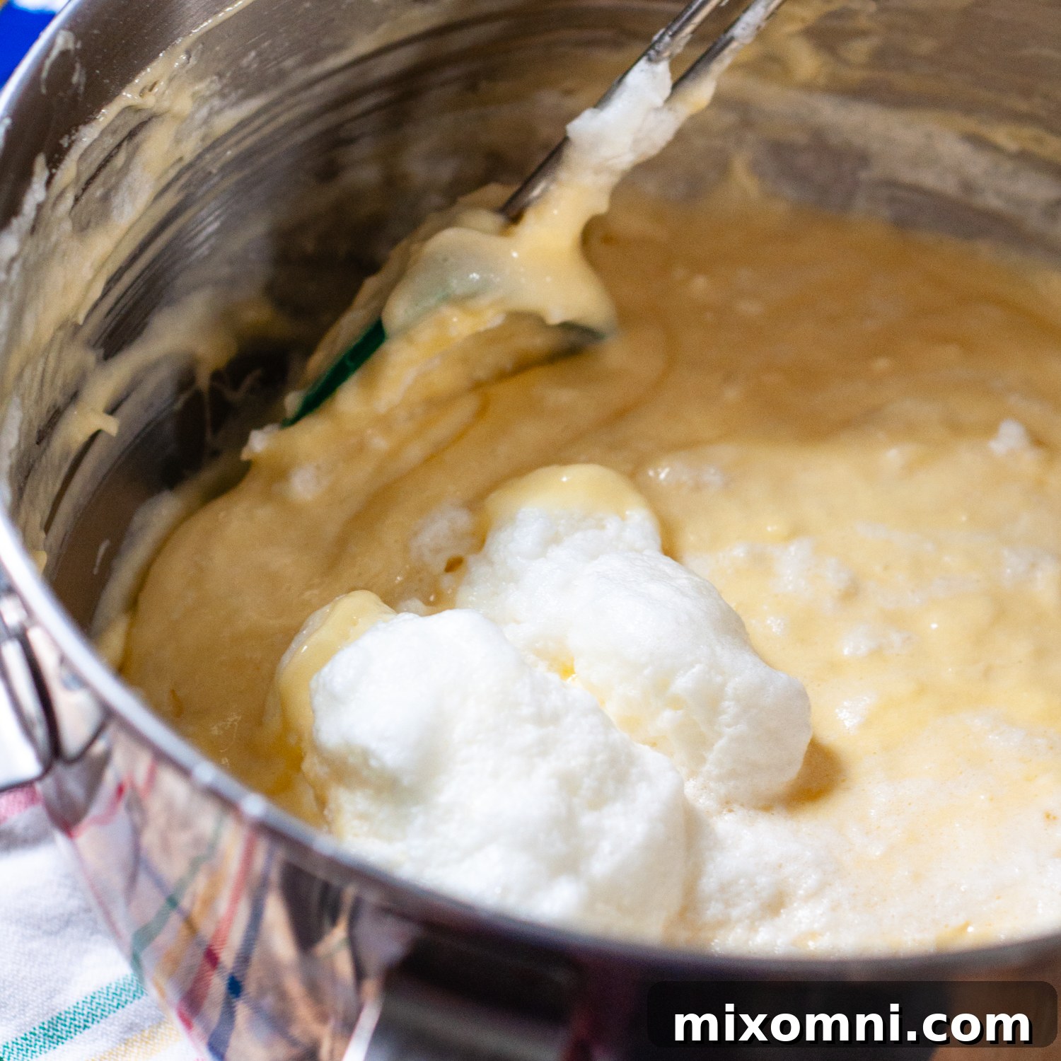 Delicately folded egg whites being incorporated into the coconut cake batter, creating an airy texture.