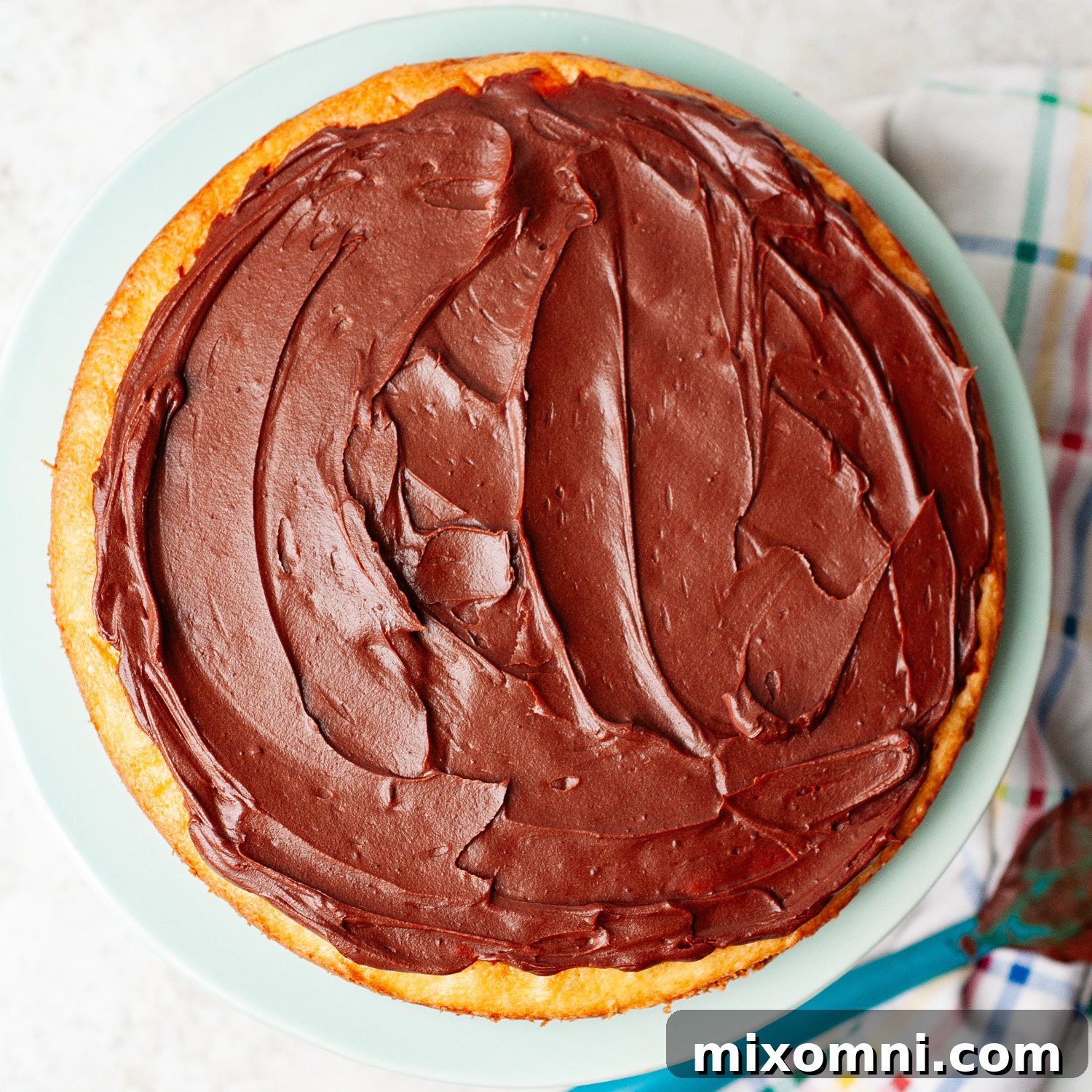 A layer of rich chocolate ganache being spread evenly over a coconut cake layer.