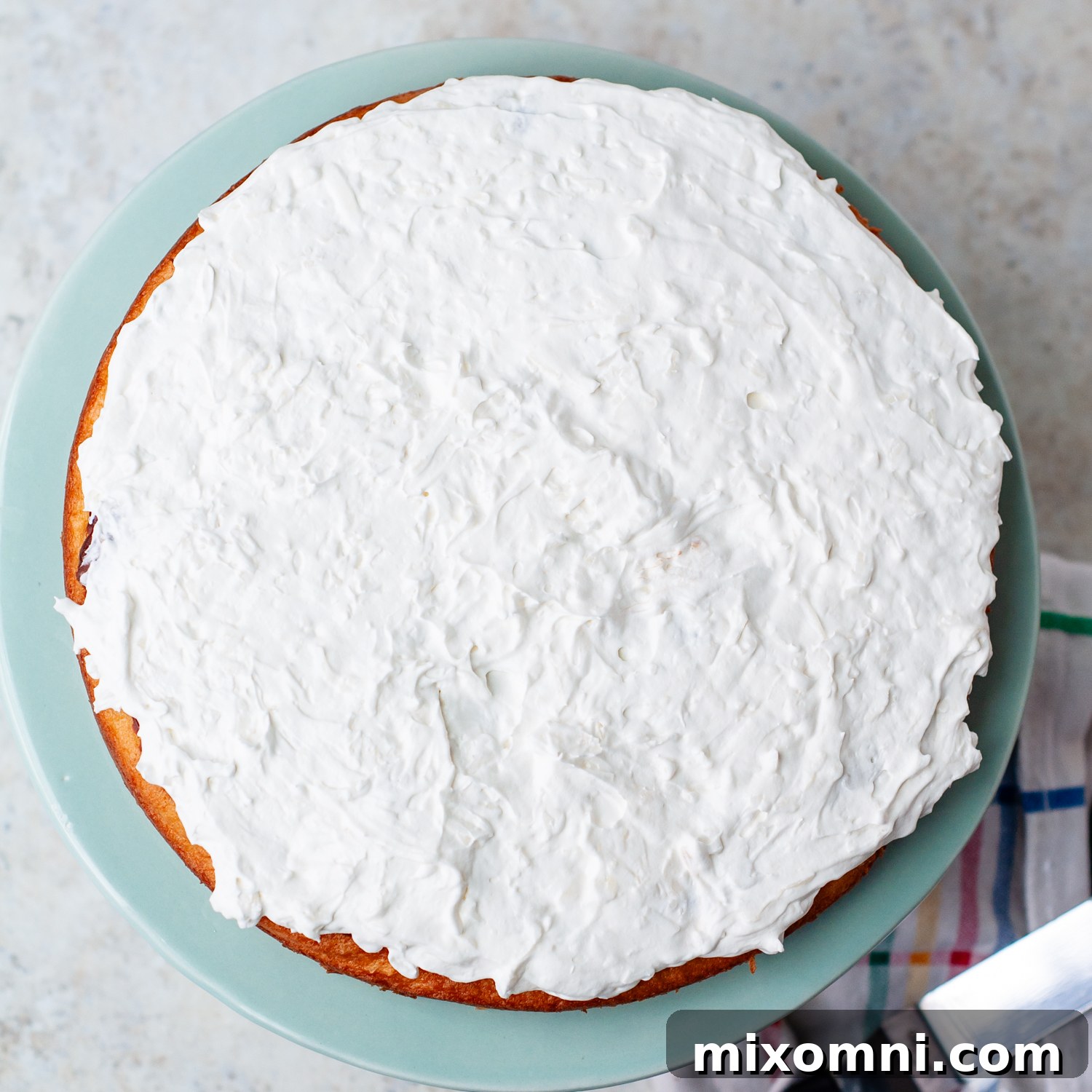 Creamy coconut frosting being spread over a cake layer, ready for the next delicious addition.