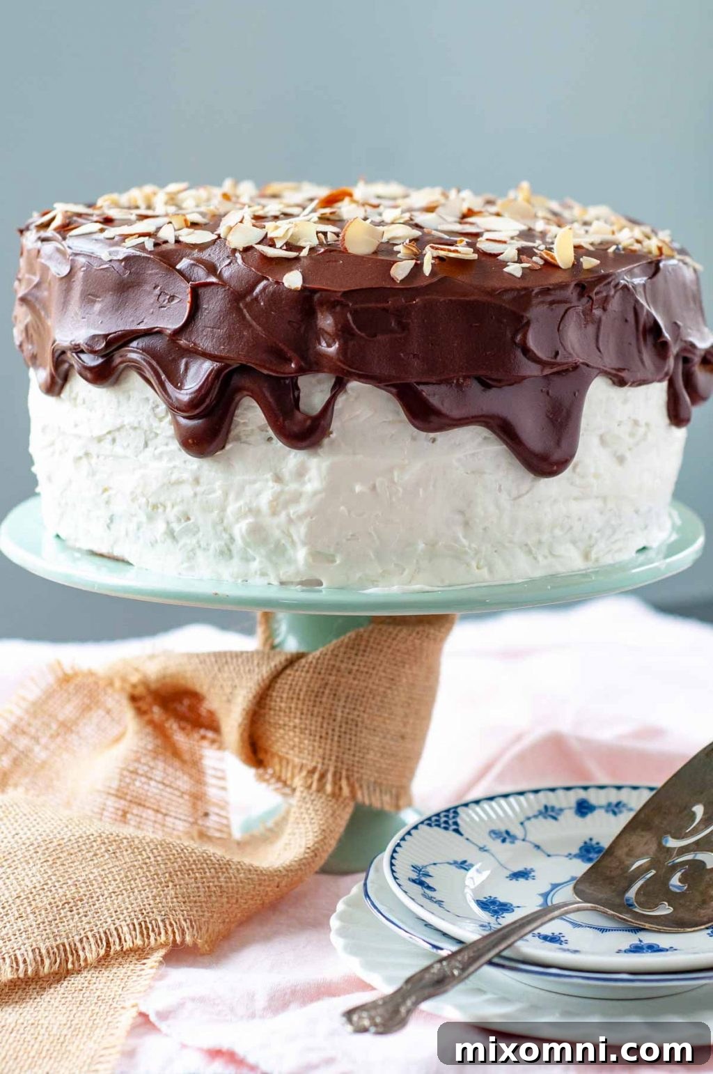 A beautifully decorated layer cake, presented on a green cake stand with a burlap ribbon, perfect for any special occasion.