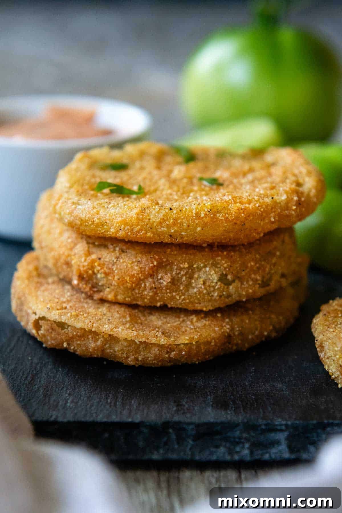 A stack of perfectly golden-brown, crispy gluten-free fried green tomatoes on a black serving tray, ready to be enjoyed.