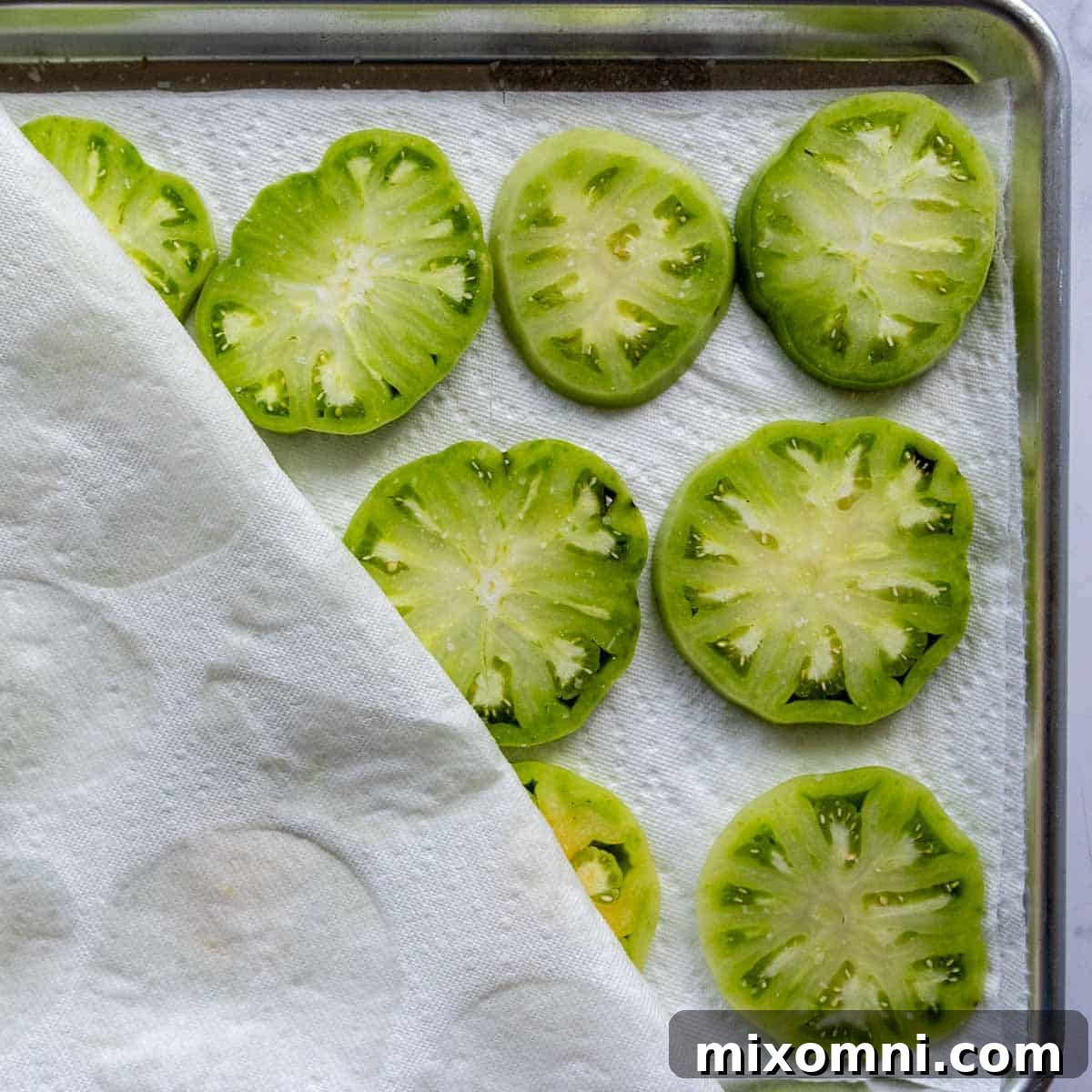 Green tomato slices lined on paper towels, lightly salted to draw out moisture for crispy frying.
