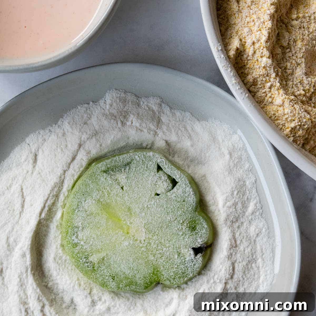 A green tomato slice lightly coated in white rice flour as part of the breading process.