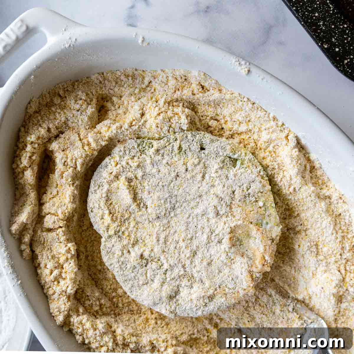 A sliced green tomato fully coated in the gluten-free cornmeal breading mixture.