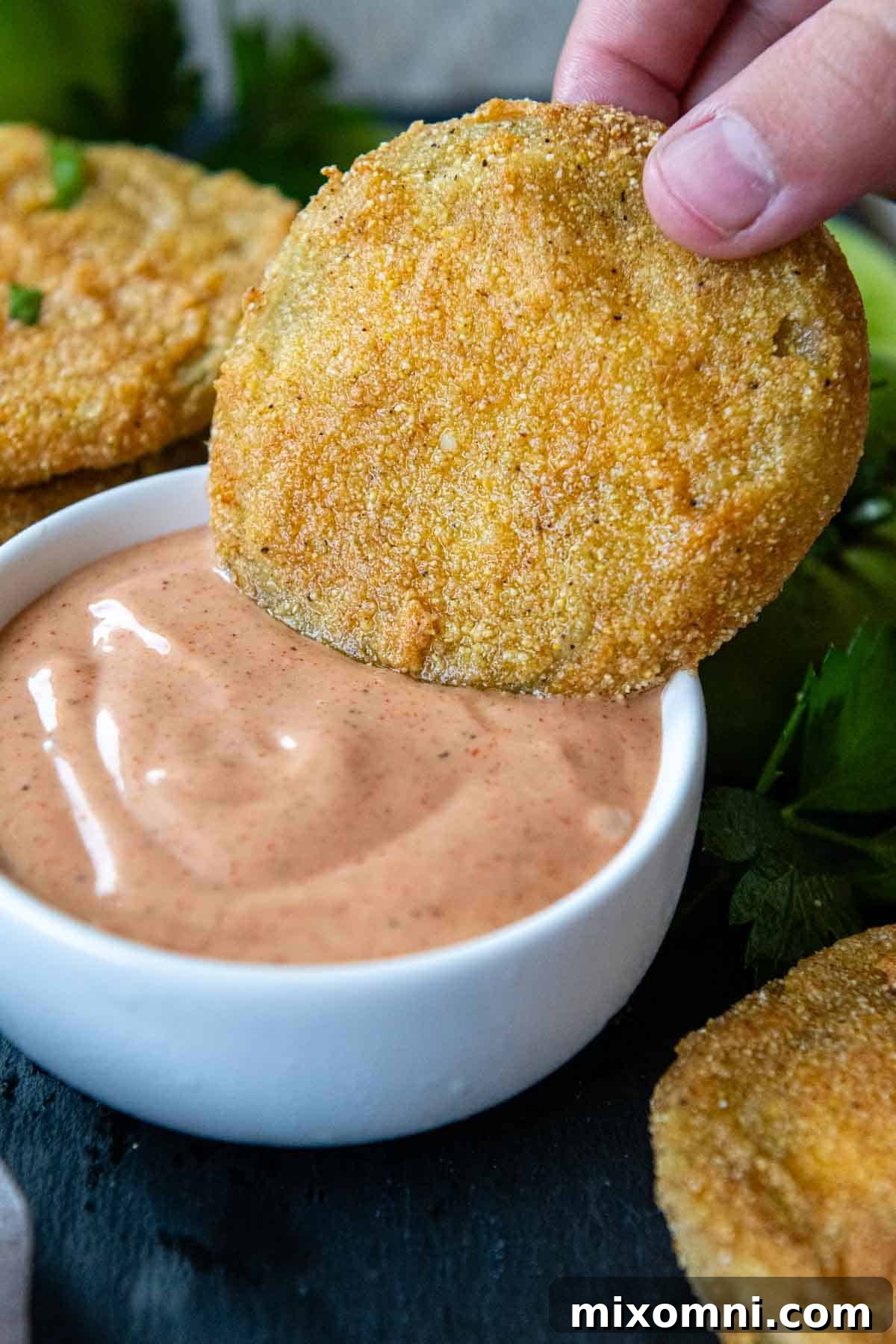 A crispy fried green tomato being dipped into a creamy, zesty comeback sauce.