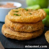 A stack of golden-brown gluten-free fried green tomatoes on a black tray.